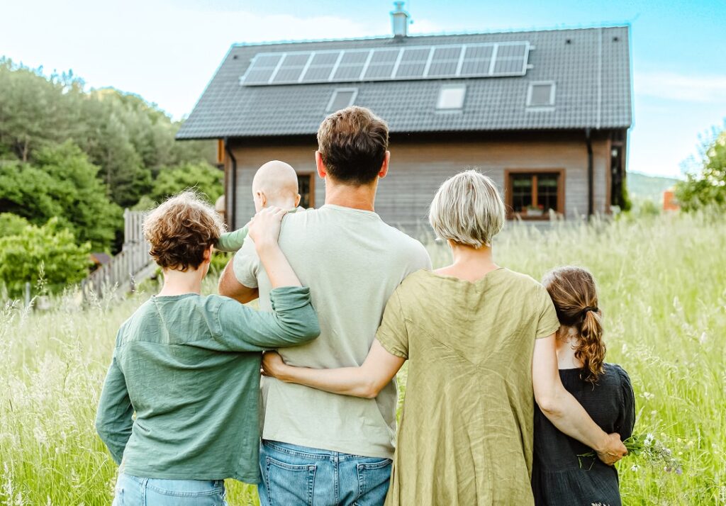 Familie steht vor einem Haus im Grünen mit einer Solaranlage auf dem Dach - Paul Energie, Ihr zuverlässiger Partner