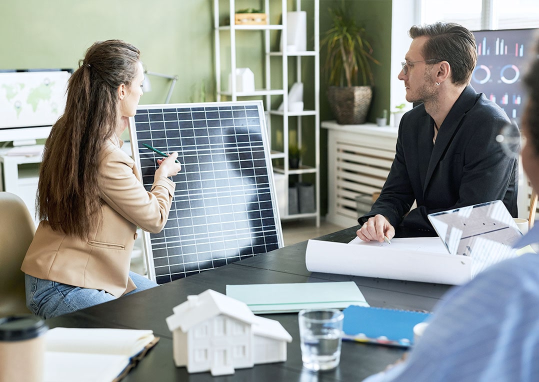 Vorteile eines Regionalen Fachpartners erklärt eine Frau mit einem Solarpanel einem Gruppe im Büro